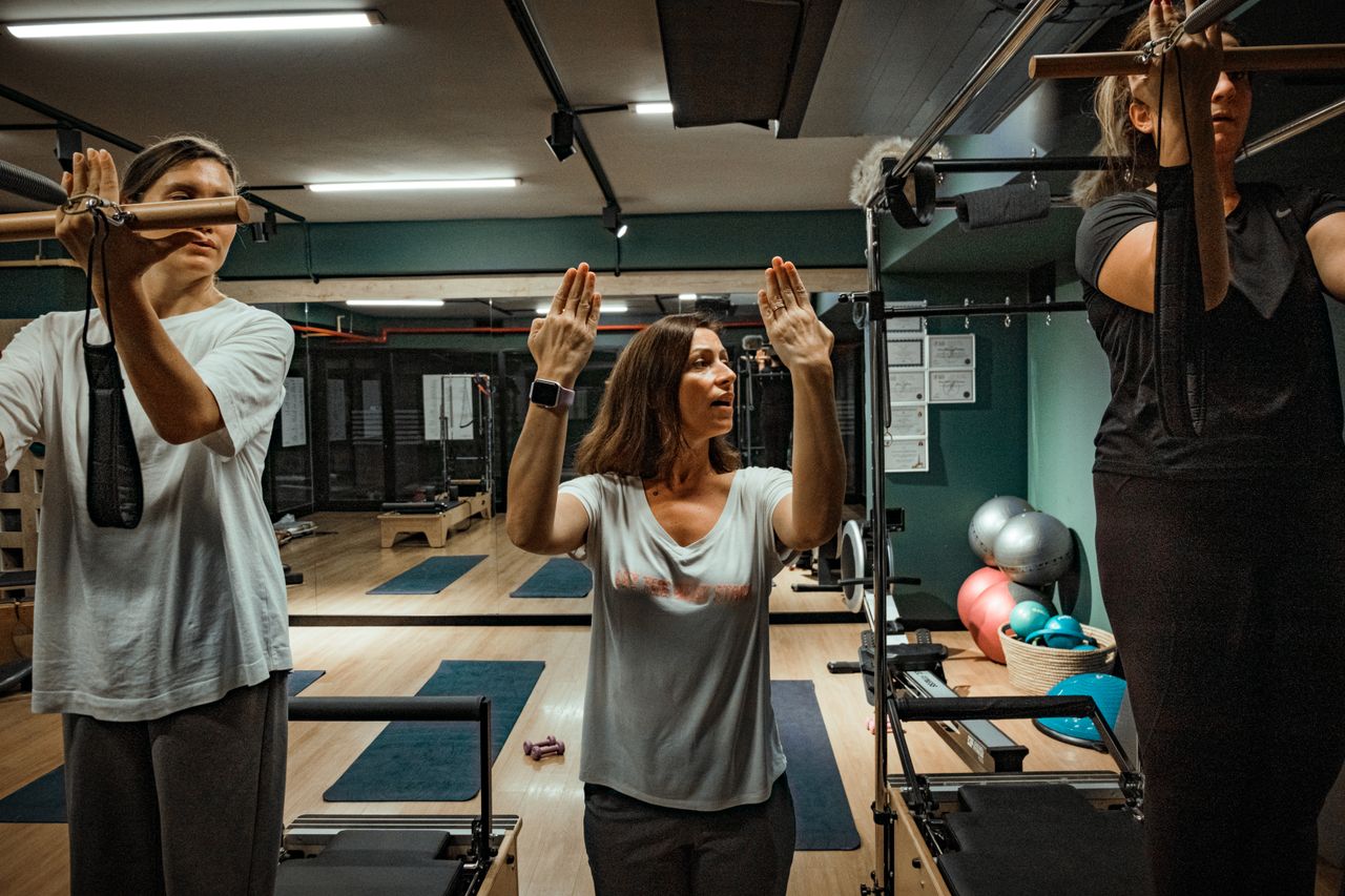 Pilates instructor guiding two women during a workout in a modern gym environment.