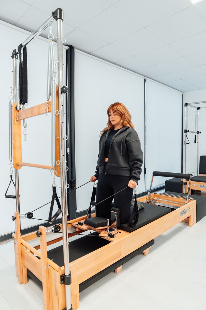 Woman practicing pilates on a tower reformer in a bright studio setting.