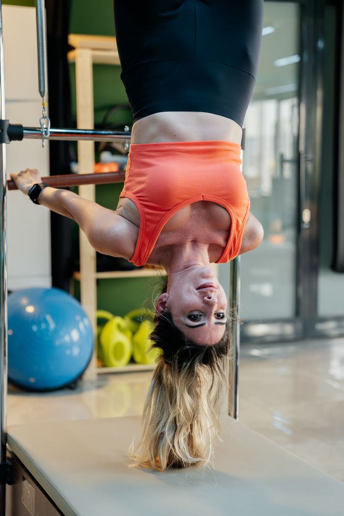 Adult woman performing an upside down pilates exercise on equipment in a gym setting.